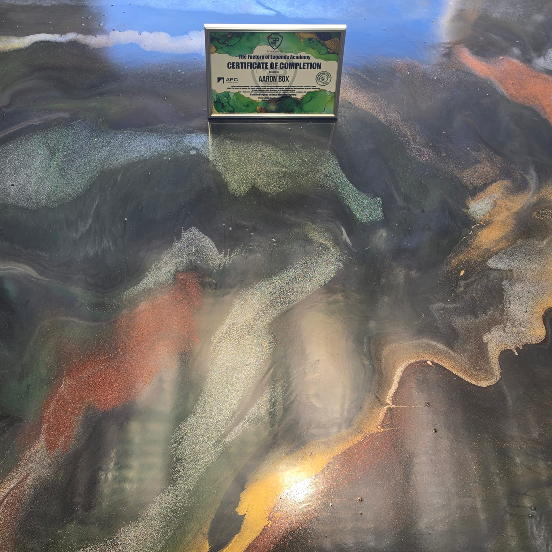 Metallic resin floor displayed with Aaron Box's resin metallic flooring certificate