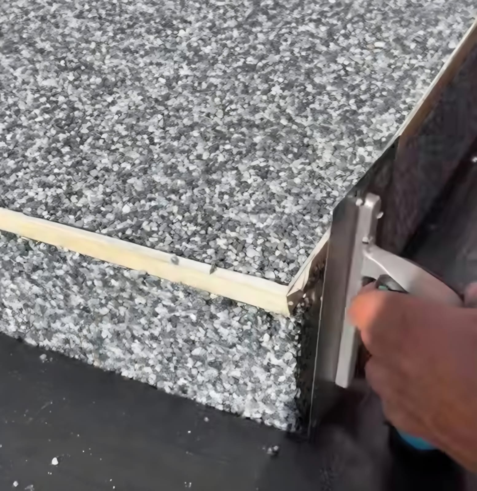 Close-up of a resin bound step edge in grey and white stone being finished by hand