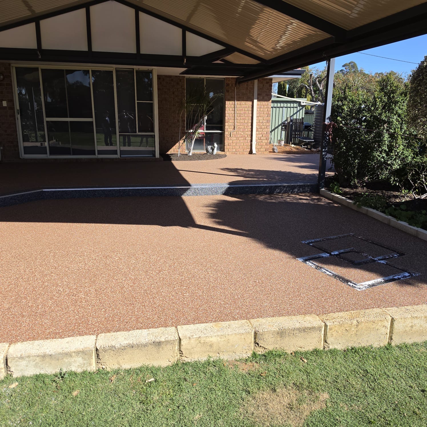Terracotta resin bound alfresco patio with charcoal border and neat drain surrounds